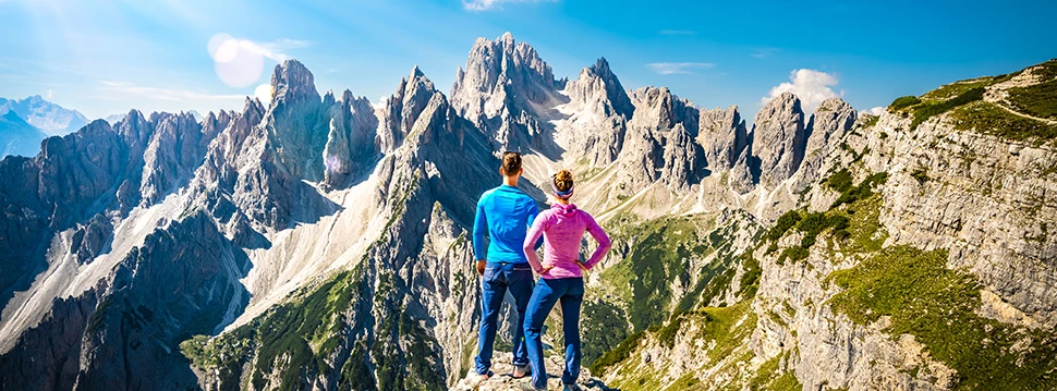 Paar steht auf Bergspitze in Tirol und blickt auf ein Bergpanorama