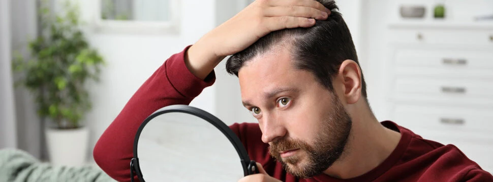 Friseur Haarverdichtung Vöcklabruck | Mann mit Haarproblemen schaut sich im Spiegel die Geheimratsecken an
