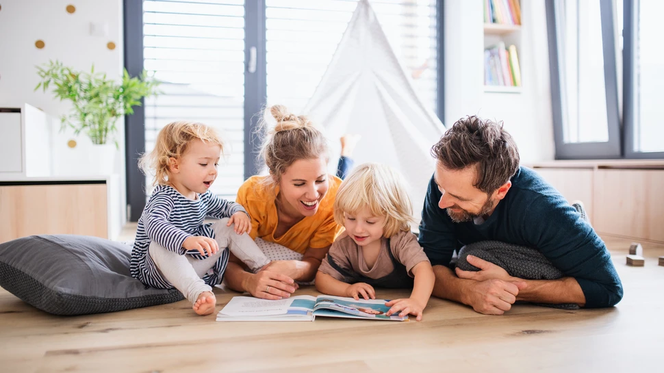 Familienzeit trägt ebenfalls zur Entschleunigung bei Familie mit zwei Kindern vertreibt sich die Zeit mit Bücherlesen. Sie liegen alle gemeinsam auf dem Boden und lachen
