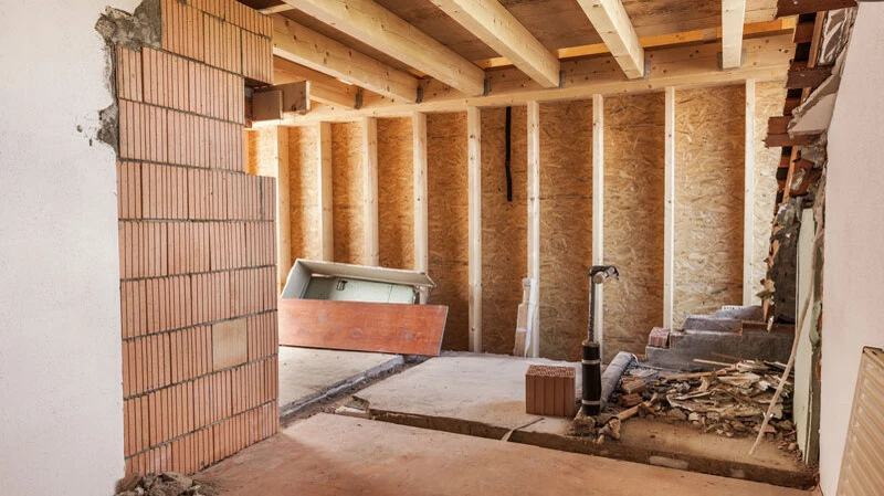 Bausanierung Rohrbach | Sanierung Renovierungsarbeiten im Innenbereich - Rohbau eines Raums mit freiliegenden Holzbalken, OSB-Platten an den Wänden, Ziegelmauerwerk und Baustellenausrüstung während der Sanierung