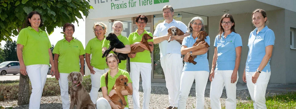 Das engagierte Team der Tierarztpraxis Reitzinger präsentiert sich vor der Praxis, gemeinsam mit ihren tierischen Patienten, unterstreicht die Verbindung von Kompetenz und Tierliebe.