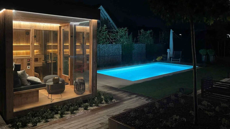 Eine beleuchtete Außensauna mit gemütlichem Loungebereich verwandelt den Garten in eine private Wellnessoase – ideal für entspannende Abende direkt neben dem Pool.
