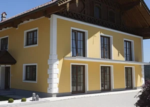 Gelber Außenputz an einem Einfamilienhaus im mediterranen Stil mit roten Dachziegeln und weißen Säulen.