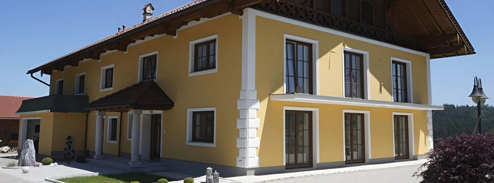 Gelber Außenputz an einem Einfamilienhaus im mediterranen Stil mit roten Dachziegeln und weißen Säulen.