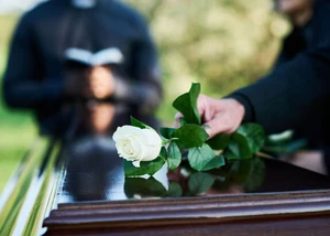 Bestattung in Leibnitz | Person legt weiße Rose auf Sarg ab