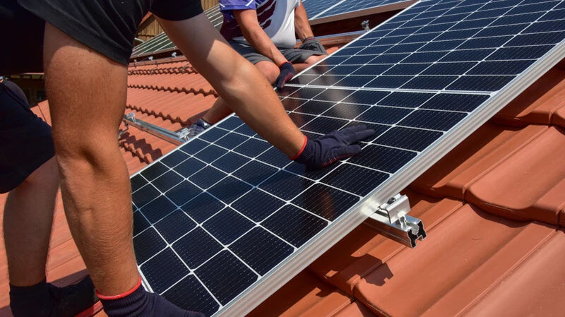 Handwerker montieren Solarmodule auf einem Ziegeldach zur Nutzung von Solarenergie.