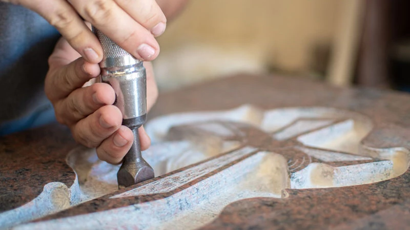 Feine Handarbeit macht jeden Grabstein zu einem Unikat – Symbole wie ein Kreuz werden mit Präzision in den Stein gearbeitet.