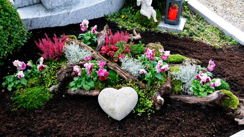 Eine liebevolle Grabgestaltung mit Herzstein, Blumen und Engelfigur schenkt Trost und macht den letzten Ruheort zu einem persönlichen Platz der Erinnerung.