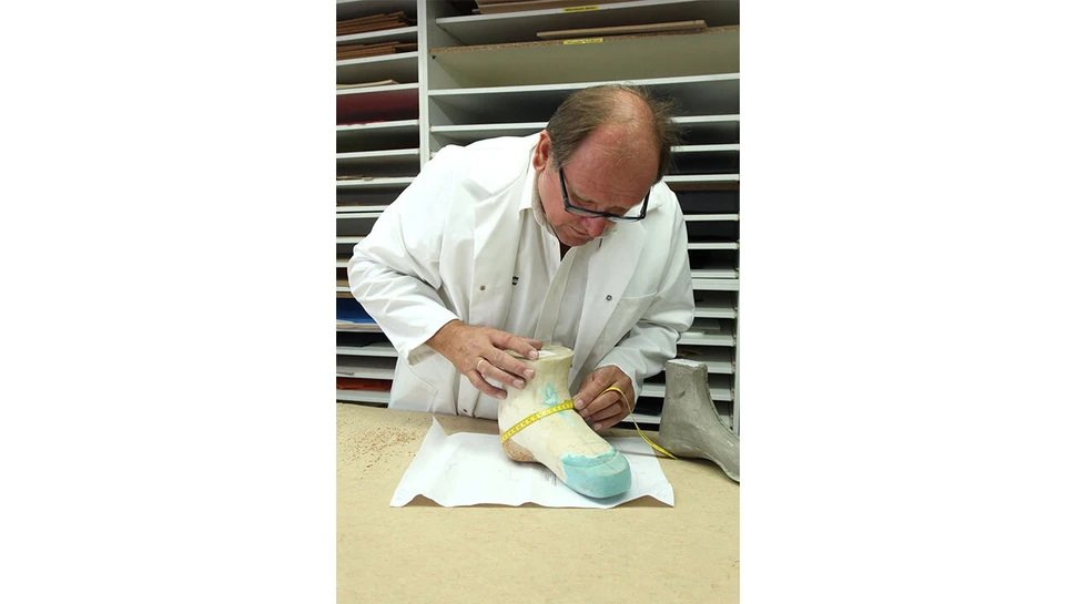 Ein Orthopädieschuhmacher der Orthopädie-Schuhtechnik Huber GmbH misst sorgfältig die Form eines Leisten, um einen individuell angepassten Schuh herzustellen.