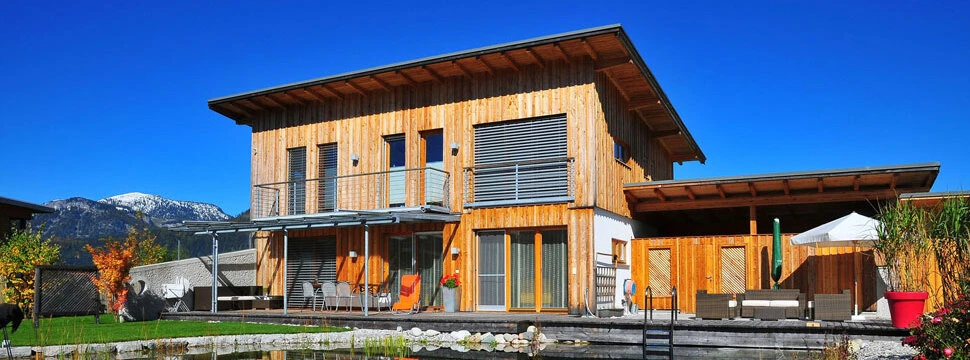 Modernes Wohnen im Einklang mit der Natur – ein Holzhaus mit klarer Architektur, großzügiger Terrasse und Schwimmteich zeigt, wie nachhaltiges Bauen und hoher Wohnkomfort zusammenfinden.