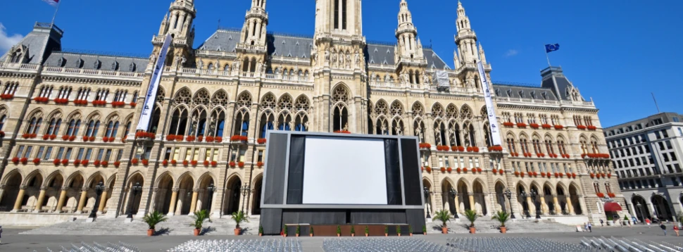 Großes gotisches Gebäude mit zahlreichen Türmen steht im Hintergrund zahlreiche Stuhlreihen und eine große Leinwand im Vordergrund klarer blauer Himmel