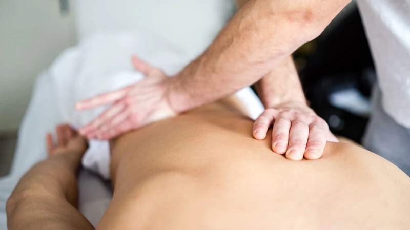 Physiotherapie Schwaz Professionelle Massage auf einer Massageliege - Therapeut führt eine Rückenmassage durch, Nahaufnahme der Massagetechnik mit beiden Händen auf dem Rücken, Wellness- und Physiotherapie-Behandlung