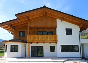 Ein modernes Einfamilienhaus im alpinen Stil mit Holzfassade und Balkon, umgeben von Bergen und Natur.