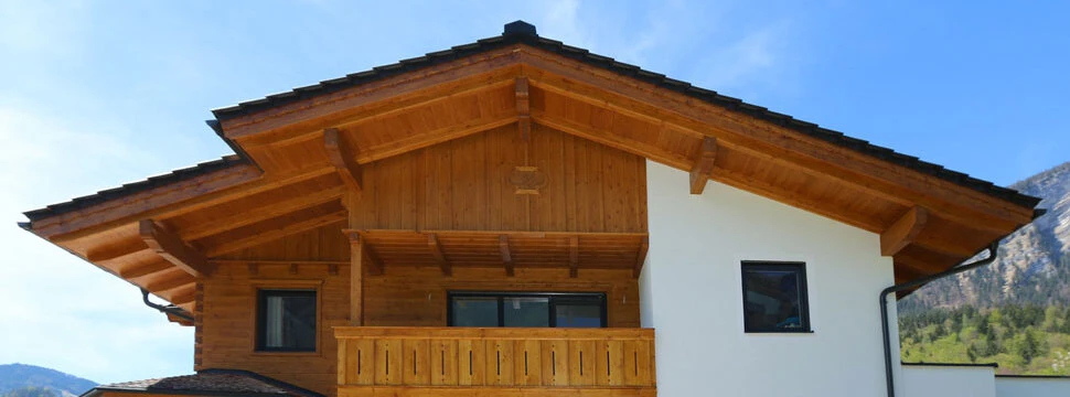 Ein modernes Einfamilienhaus im alpinen Stil mit Holzfassade und Balkon, umgeben von Bergen und Natur.