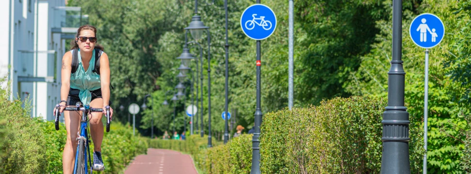 Frau fährt auf Radweg in einer grünen, städtischen Umgebung