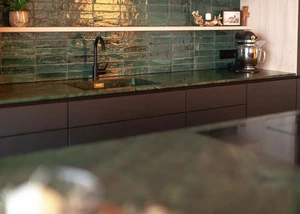 Grüne Naturstein-Küchenarbeitsplatte mit schwarzen Armaturen und glänzenden grünen Wandfliesen in einer modernen Küche.