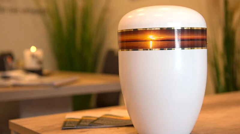 Weiße Urne mit Sonnenuntergangsmotiv auf einem Tisch